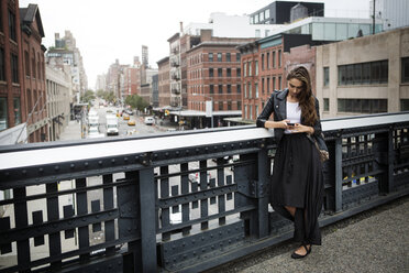 Woman using mobile phone while standing on bridge in city - CAVF22390