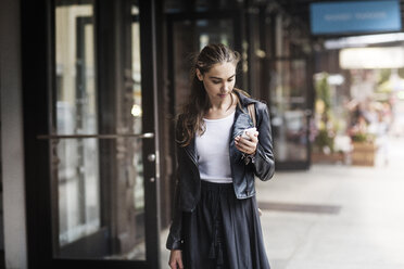 Front view of woman using phone while standing on sidewalk - CAVF22394