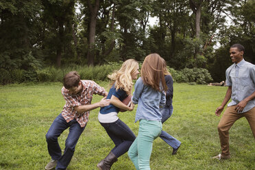 Cheerful friends playing football on grassy field - CAVF22418