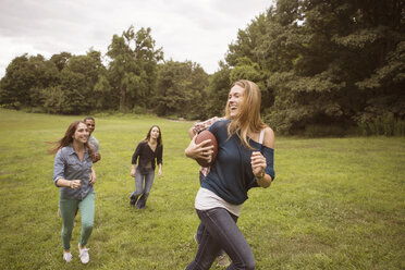 Verspielte Freunde jagen eine Frau, die einen Fußball auf einer Wiese hält - CAVF22419