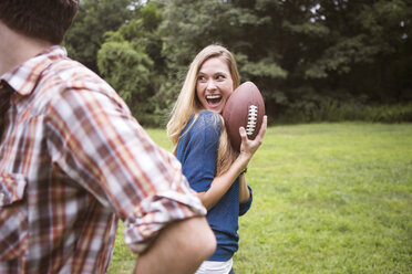 Fröhliche Frau, die einen Fußball hält, während ein Mann auf einer Wiese steht - CAVF22427