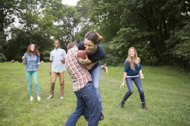 Mann verteidigt Frau, die einen Fußball hält, während Freunde sie auf dem Spielfeld beobachten - CAVF22430
