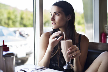 Frau schaut weg, während sie einen Schokoladenmilchshake im Café hält - CAVF22441
