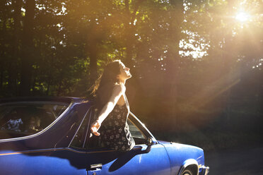 Woman with arm outstretched leaning out of pick-up truck window in forest - CAVF22457