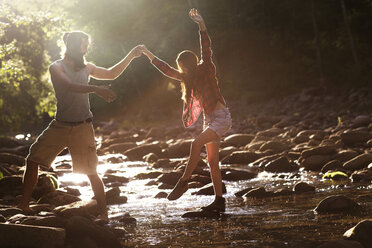 Boyfriend holding girlfriend while crossing stream in forest - CAVF22460