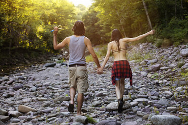 Rear view of couple holding hands while walking on rocks in forest - CAVF22461