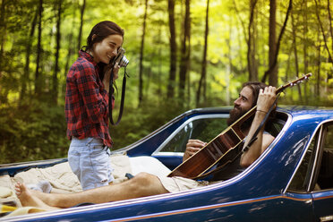 Frau fotografiert Freund mit Gitarre in Pick-up-Truck im Wald - CAVF22470