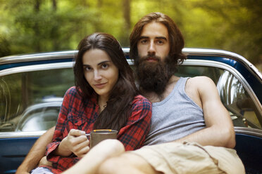 Portrait of confident couple sitting in pick-up truck in forest - CAVF22471
