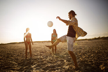 Freunde spielen Fußball am Strand gegen den Himmel - CAVF22482