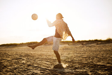 Mann spielt Fußball am Strand bei Sonnenuntergang - CAVF22483