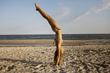 Seitenansicht der Frau macht Handstand am Strand gegen den Himmel - CAVF22484