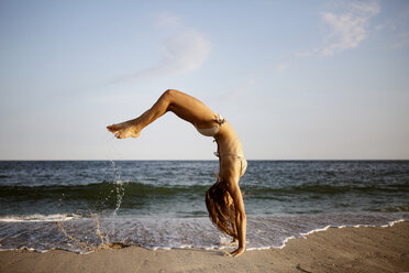 Side view of woman doing back flip at beach against sky - CAVF22486