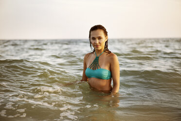 Porträt einer selbstbewussten Frau, die ein blaues Bikinioberteil trägt und im Meer steht - CAVF22490