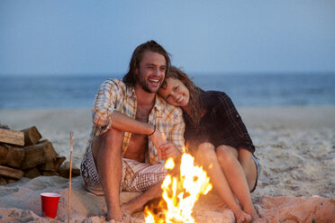 Fröhliches Paar sitzt am Strand am Lagerfeuer - CAVF22496