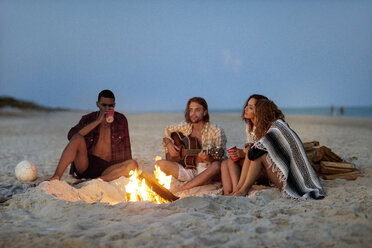 Friends sitting by bonfire at beach - CAVF22497