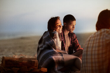 Happy woman sitting with man on beach at dusk - CAVF22498