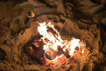 Blick von oben auf Marshmallows in Spießen über Lagerfeuer am Strand - CAVF22500