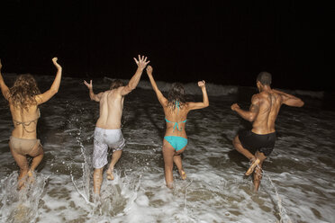 Rear view of friends running in sea at night - CAVF22503