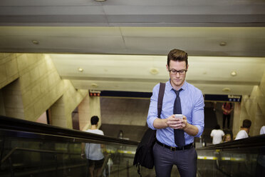 Businessman using smart phone while standing on escalator in subway station - CAVF22508