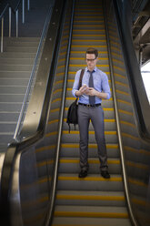 Geschäftsmann, der ein Smartphone benutzt, während er auf einer Rolltreppe in einer U-Bahn-Station steht - CAVF22518