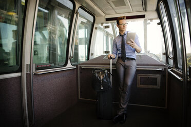 Geschäftsmann hält Tablet-Computer und Gepäck in einem Zug stehend - CAVF22522