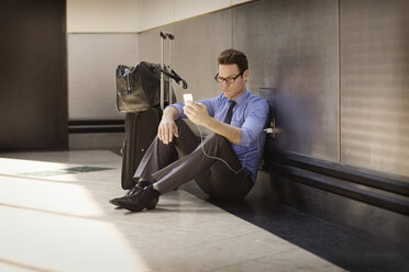 Geschäftsmann lädt sein Smartphone auf, während er in der U-Bahn-Station auf dem Boden sitzt - CAVF22531