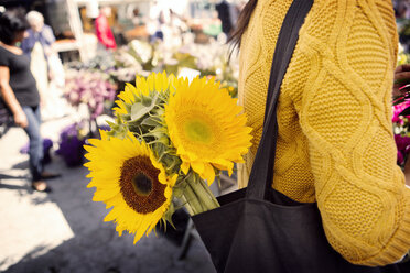 Mittelteil einer Frau mit Sonnenblumen in der Handtasche auf dem Markt - CAVF22558