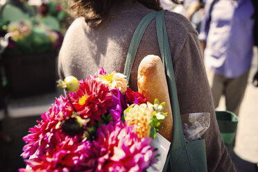 Mittelteil einer Frau mit Blumen und Brot in der Handtasche auf dem Markt - CAVF22561