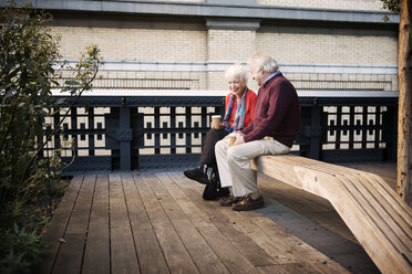 Happy senior couple sitting on wooden bench at patio - CAVF22564