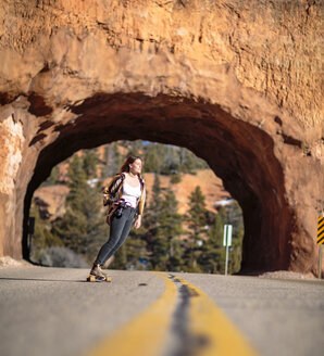 Female hiker skateboarding on road against rocky tunnel at Bryce Canyon National Park - CAVF22577