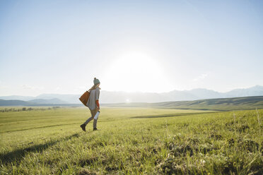 Rear view of female hiker walking on grassy field against clear sky - CAVF22605