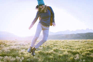 Weibliche Wanderin springt auf grasbewachsenem Feld gegen den Himmel - CAVF22610