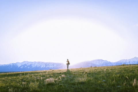 Weibliche Wanderin auf grasbewachsenem Feld vor Bergen stehend, lizenzfreies Stockfoto