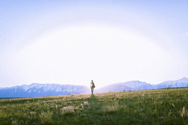 Female hiker standing on grassy field against mountains - CAVF22612