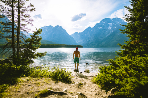 Rückansicht eines Mannes, der auf einem Felsen am See stehend die Aussicht betrachtet, lizenzfreies Stockfoto