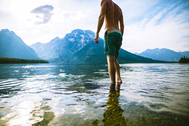 Low section of man standing in lake against mountains and sky - CAVF22615