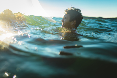 Glücklicher Mann schwimmt im Meer gegen den Himmel, lizenzfreies Stockfoto