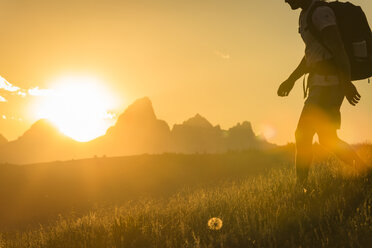 Niedriger Ausschnitt eines Wanderers mit Rucksack, der bei Sonnenuntergang auf einer Wiese gegen die Berge läuft - CAVF22630