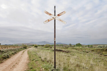 Abandoned road sign by dirt road against cloudy sky - CAVF22660