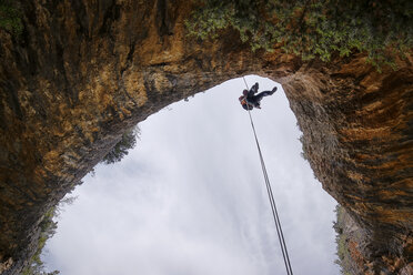 Low angle view of man rappelling from mountain - CAVF22687