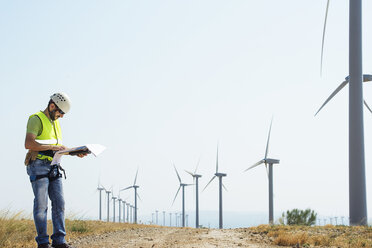 Engineer reading documents at wind farm against sky - CAVF22702