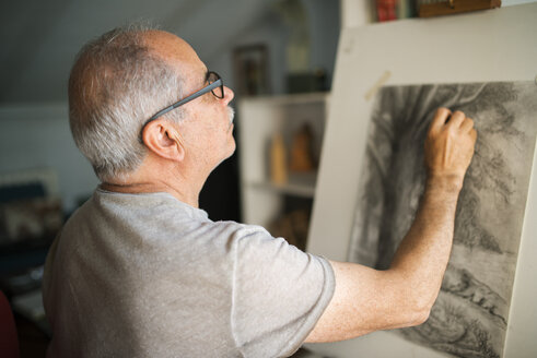 Konzentrierter älterer Mann, der zu Hause auf einer Leinwand skizziert - CAVF22711
