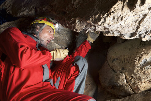 Niedriger Blickwinkel eines Archäologen, der in einer Höhle sitzend Felsen bearbeitet - CAVF22725
