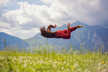 Woman in mid-air over grassy field against mountains - CAVF22750