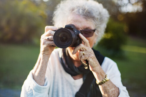 Nahaufnahme einer älteren Frau, die im Park durch eine Kamera fotografiert - CAVF22760