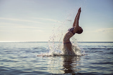 Verführerische Frau spritzt Wasser beim Tauchen ins Meer gegen den Himmel - CAVF22787