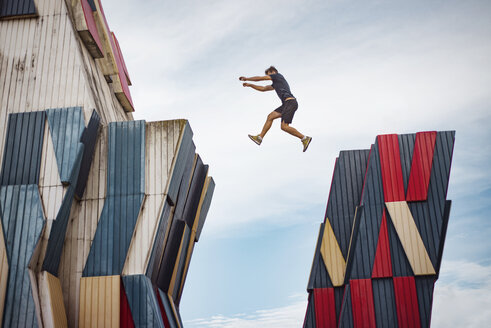 Low angle view of man jumping over buildings against sky - CAVF22810