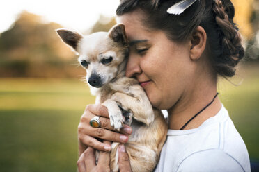 Seitenansicht einer lächelnden Frau, die einen Chihuahua auf einem Feld hält - CAVF22822