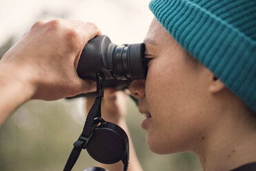 Seitenansicht einer Frau, die im Wald durch ein Fernglas schaut - CAVF22825