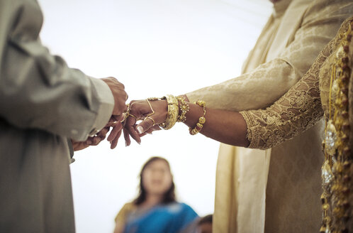 Priester bindet die Finger von Braut und Bräutigam während der Hochzeitszeremonie - CAVF22828